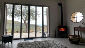 A spacious room with a large sliding glass door leading to an outdoor area, a fireplace, and a round mirror on the wall. - Modern architect's house in olive grove with sea views (Vasia)