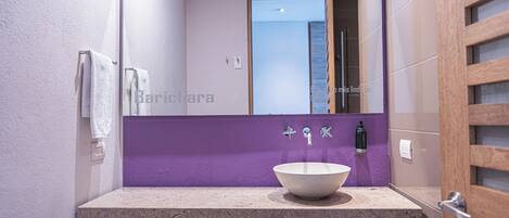A bathroom with a large mirror, a white sink, and a purple accent wall.