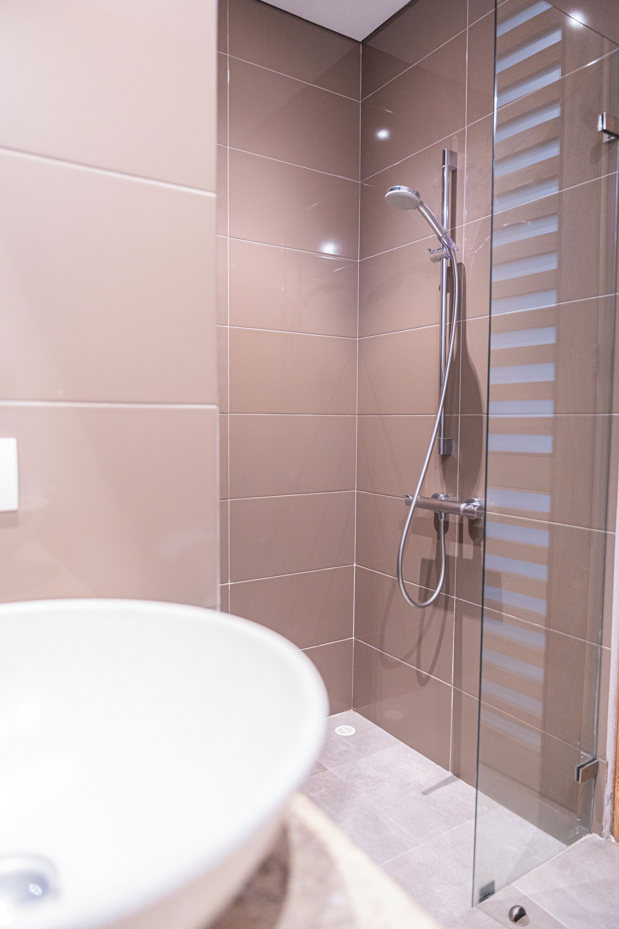 Un baño con cabina de ducha de vidrio, un lavabo blanco y suelo de baldosas.