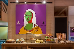 Experience the vibrant atmosphere of our lobby, featuring a stunning mural and a buffet counter with a variety of food options.