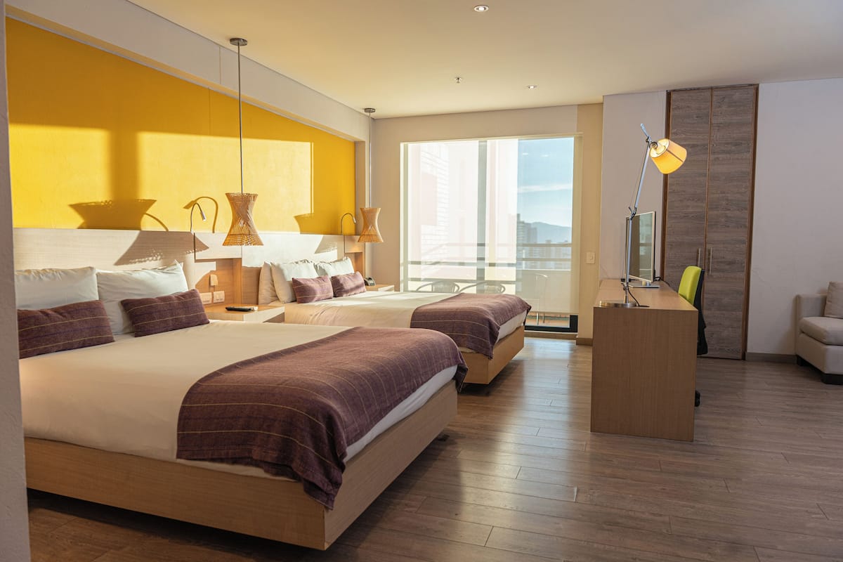 A modern hotel room with two large beds, a desk, and a view of the city.