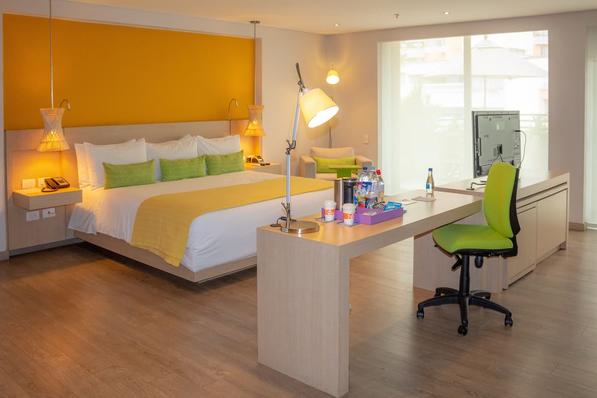 A modern hotel room with a large bed, bedside lamps, a desk with a chair, and a computer.
