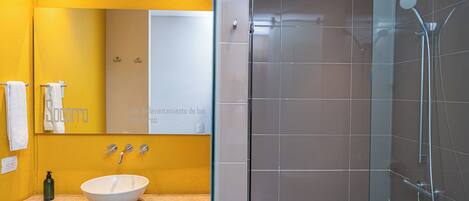 A modern bathroom with a large mirror, a white sink, and a glass-enclosed shower.