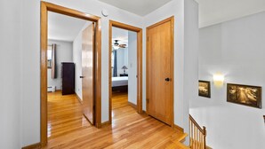 A hallway with wooden flooring, white walls, and a staircase with a wooden railing. - Cheerful 3 bedroom. Feels like home. (Chicago)