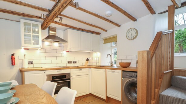 A compact kitchen with white cabinets, a built-in oven, and a washing machine. - 3 Settlebeck Cottages (Sedbergh)