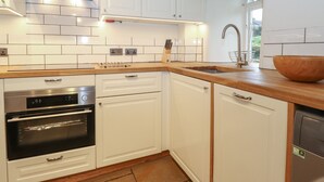 A modern kitchen with white cabinets, a stainless steel range hood, a built-in oven, and a dishwasher. - 3 Settlebeck Cottages (Sedbergh)