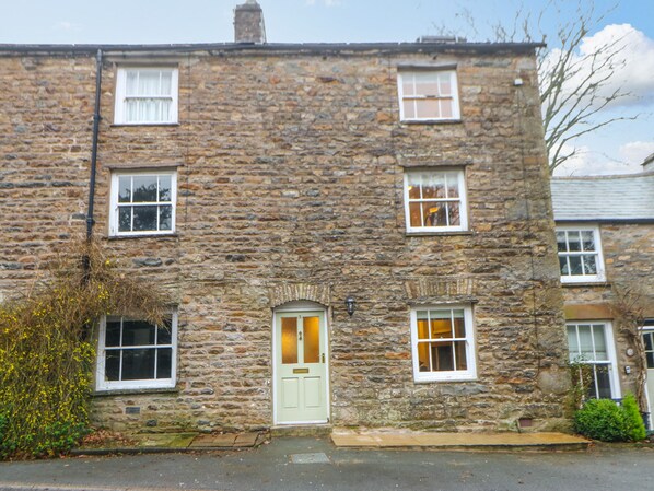 A stone building with a green door, multiple windows, and a small garden area with yellow flowers.