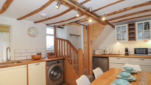 A kitchen with wooden beams, a washing machine, a dining table with blue plates, and a clock on the wall. - 3 Settlebeck Cottages (Sedbergh)