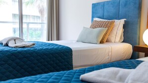 Ein Hotelzimmer mit zwei Betten, einem blauen Kopfteil und Blick auf Palmen.