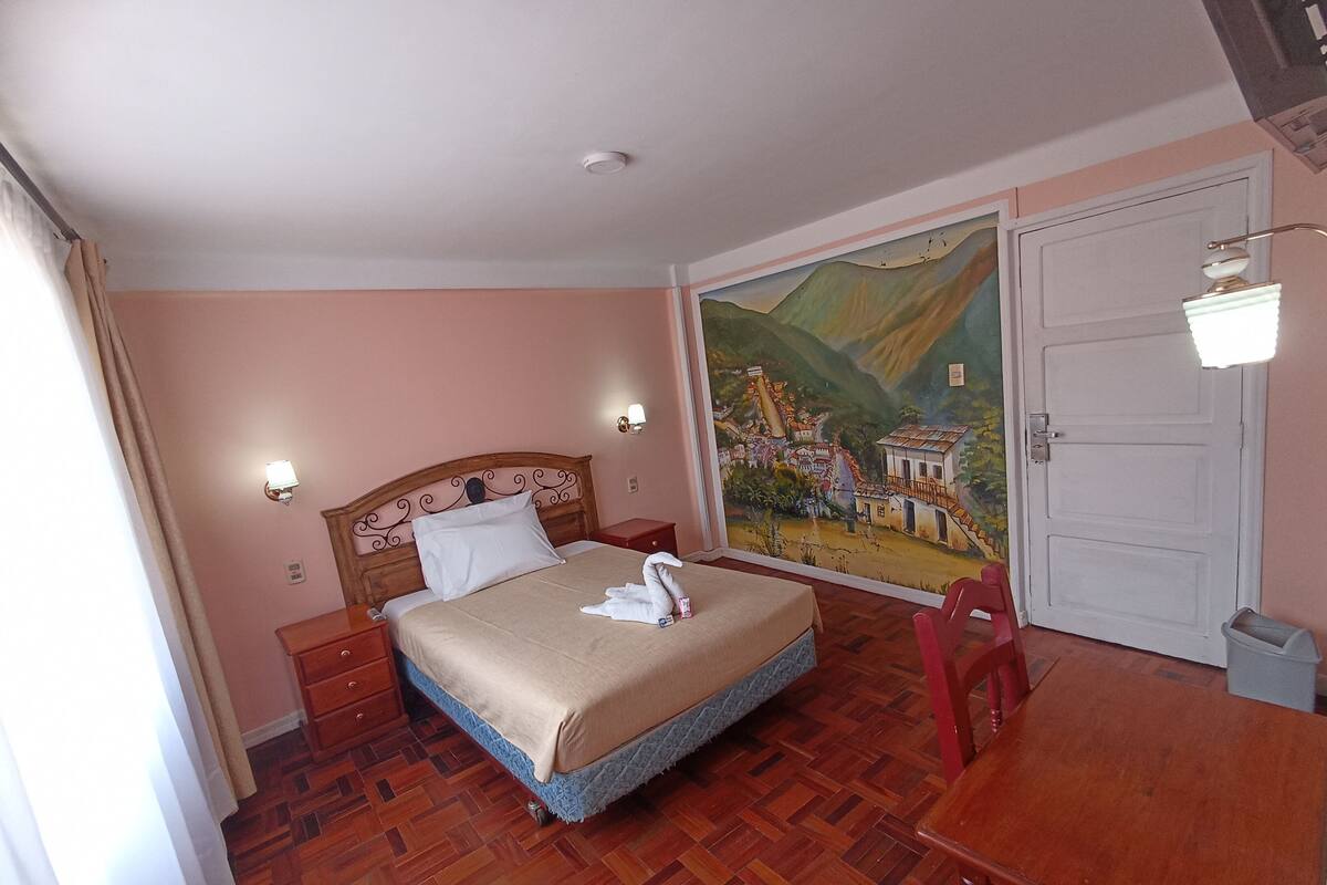 A bedroom with a bed, nightstands, a desk, a chair, a door, and a mural on the wall.