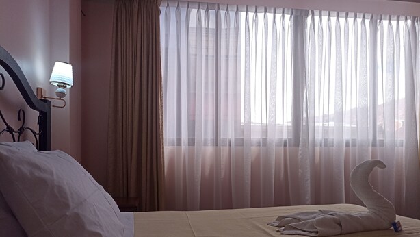 A hotel room with a bed, a lamp, sheer curtains, and a swan-shaped towel on the bed. - RIXAA Hotel (La Paz)