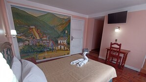 A hotel room with a bed, a chair, a desk, a TV, and a mural on the wall. - RIXAA Hotel (La Paz)