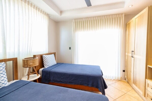 A room with two beds, a wooden wardrobe, and a window with curtains.