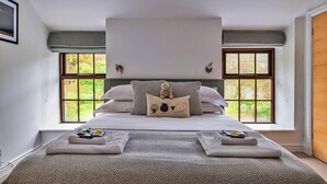 Una camera da letto con un letto grande, due finestre, una testiera e vista sul verde.