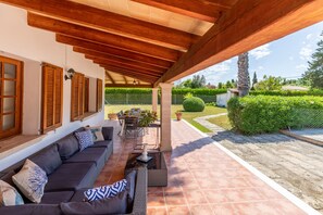 An outdoor patio with a covered seating area, a dining table, and a view of a well-maintained garden.