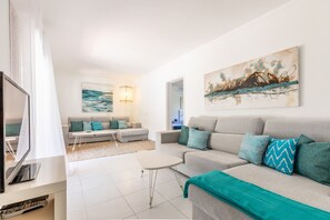 A modern living room with a grey sofa, teal cushions, and a white coffee table. - Villa Vora by JS Villas (Port de Pollença)
