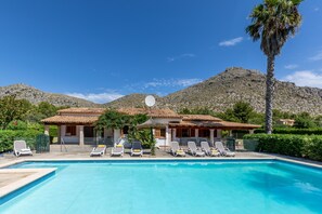A pool with sun loungers and a house with a tiled roof.