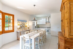 A spacious kitchen with white cabinetry, a dining table, and a large wooden cabinet.