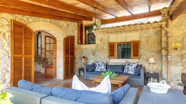 A cozy outdoor seating area with wicker furniture, stone walls, and wooden beams. - Villa Costa by JS Villas (Port de Pollença)