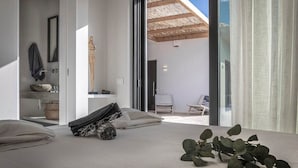 Een moderne slaapkamer met een groot bed, uitzicht op het omliggende landschap, een klein zithoekje en een minimalistische badkamer.