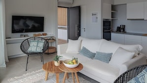 Een moderne woonkamer met een witte bank, een televisie, een eethoek met een tafel en stoelen, en een keuken met kasten en apparatuur.