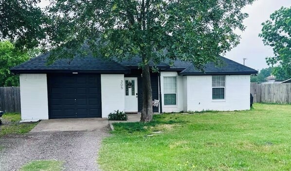 A single-story house with a black garage door, a small front yard, and a tree in front. - Cozy quiet home (Palmer)