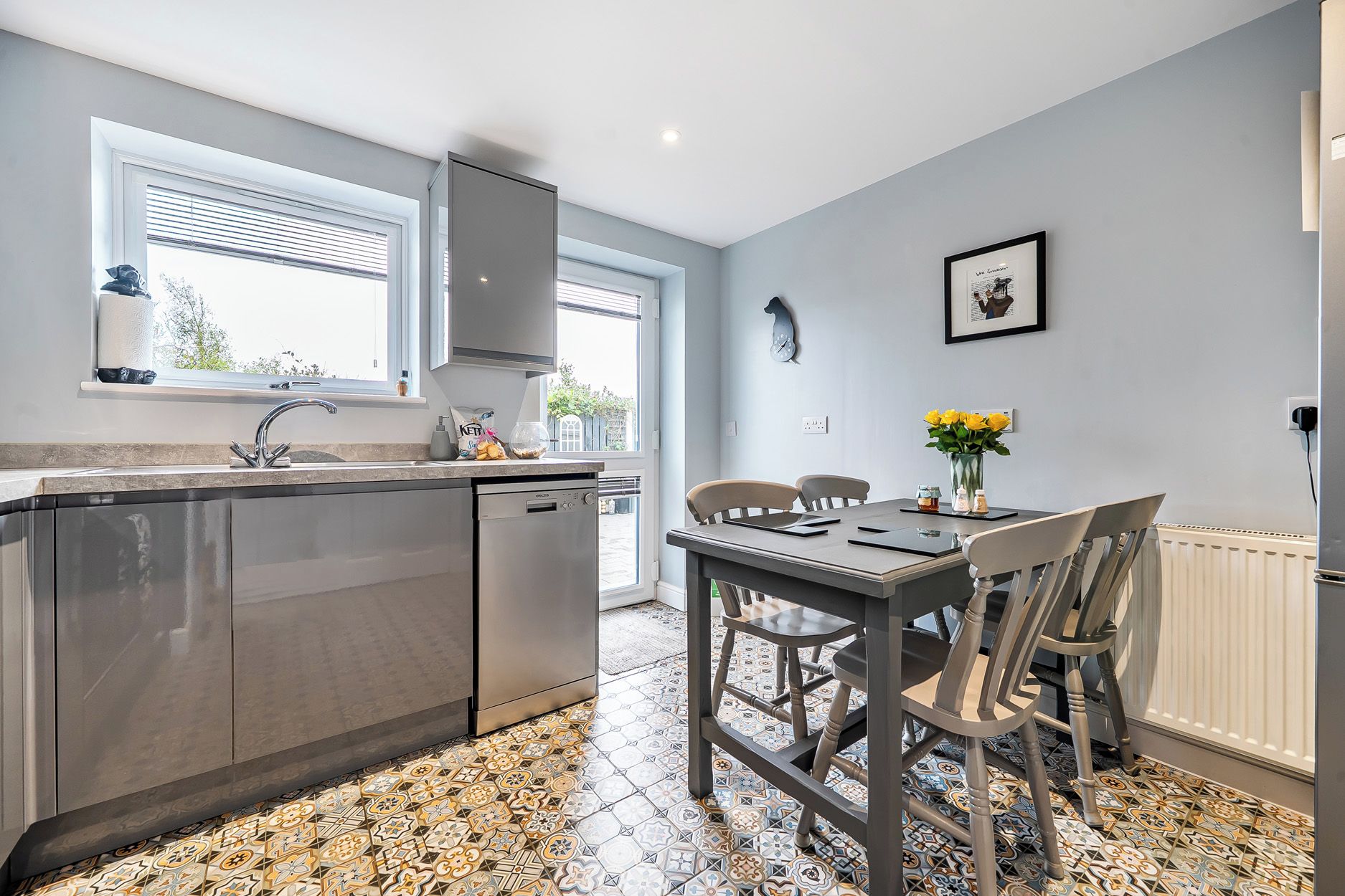 A modern kitchen with a built-in dishwasher, a dining table with chairs, and a patterned floor.