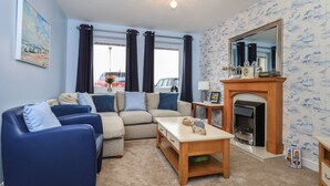 Una sala de estar con un sofá azul, un sofá beige y una mesa de centro de madera. Hay una chimenea con un espejo encima y una ventana con cortinas.