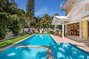 A rectangular swimming pool with a white deck, surrounded by lush greenery and trees. - Family Getaway at The Sea Zoo - Bayfront with Pool, Tiki Bar, and Games! (Bradenton Beach)