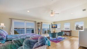 Ein Schlafzimmer mit einem großen Bett, einem Schreibtisch, einem Stuhl, einem Fernseher und einem Balkon mit Meerblick.