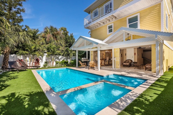 Una casa de dos pisos con piscina, mobiliario exterior y un porche cubierto.