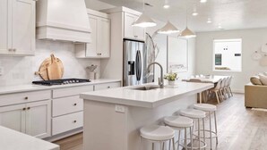 Una cucina moderna con mobili bianchi, un'isola centrale con sgabelli, un frigorifero in acciaio inossidabile e luci a sospensione.