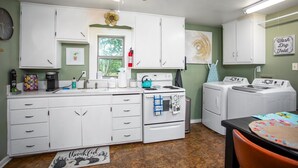 Una cocina compacta con armarios blancos, estufa, pileta y lavadora.