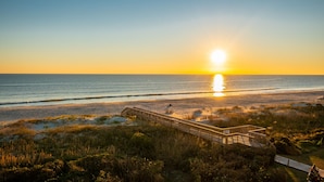 A wooden boardwalk leading to a beach with the sun setting over the ocean. - Changing Tides: Tastefully Decorated Condo with Community Pool and Easy Beach Ac (Caswell Beach)