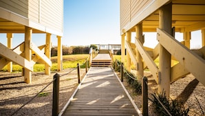 A wooden pathway leading to a building with a covered entrance and a staircase. - Changing Tides: Tastefully Decorated Condo with Community Pool and Easy Beach Ac (Caswell Beach)