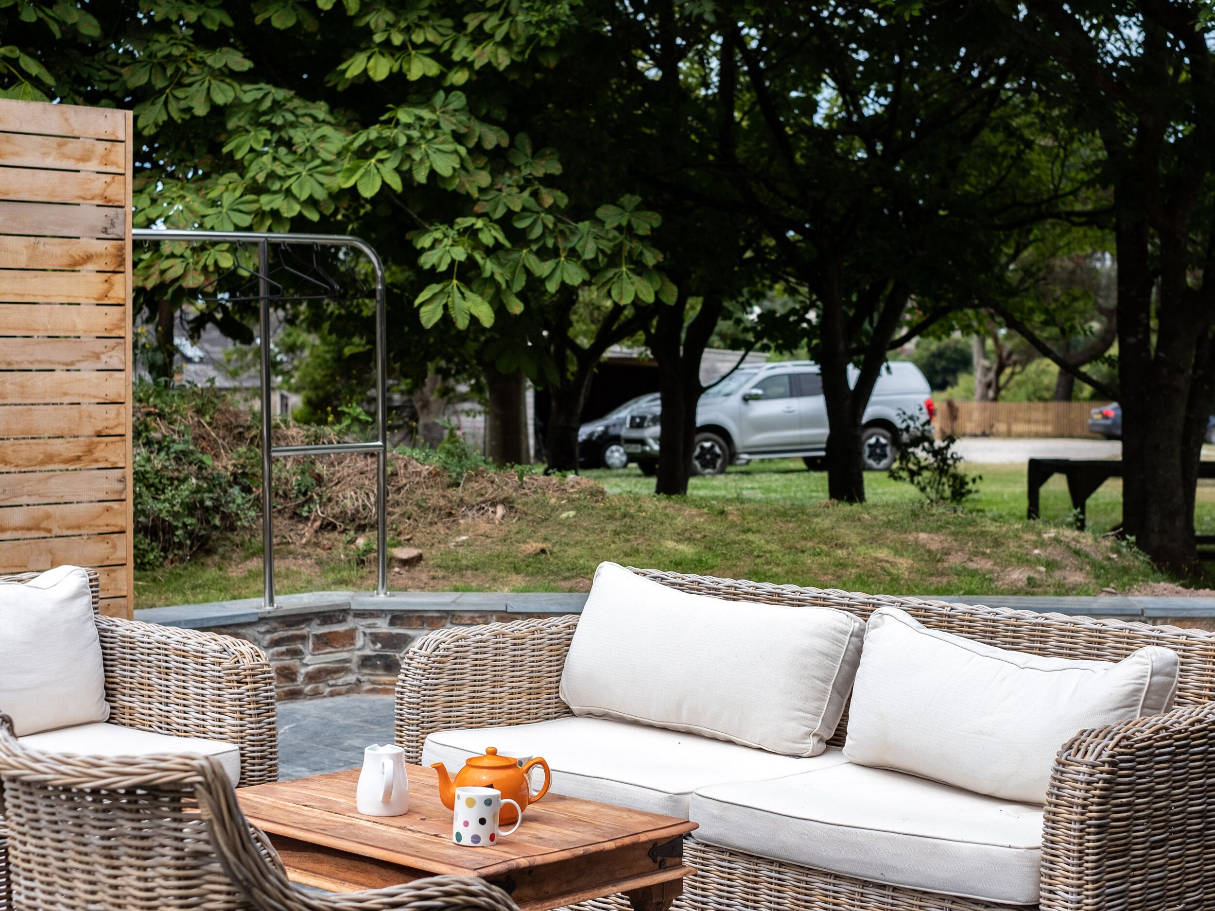 An outdoor seating area with wicker furniture and a table with a teapot and mug.