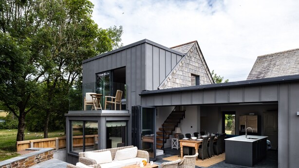 A modern house with a patio area featuring outdoor furniture, a grill, and a dining table. - Porthilly Greys (Wadebridge)