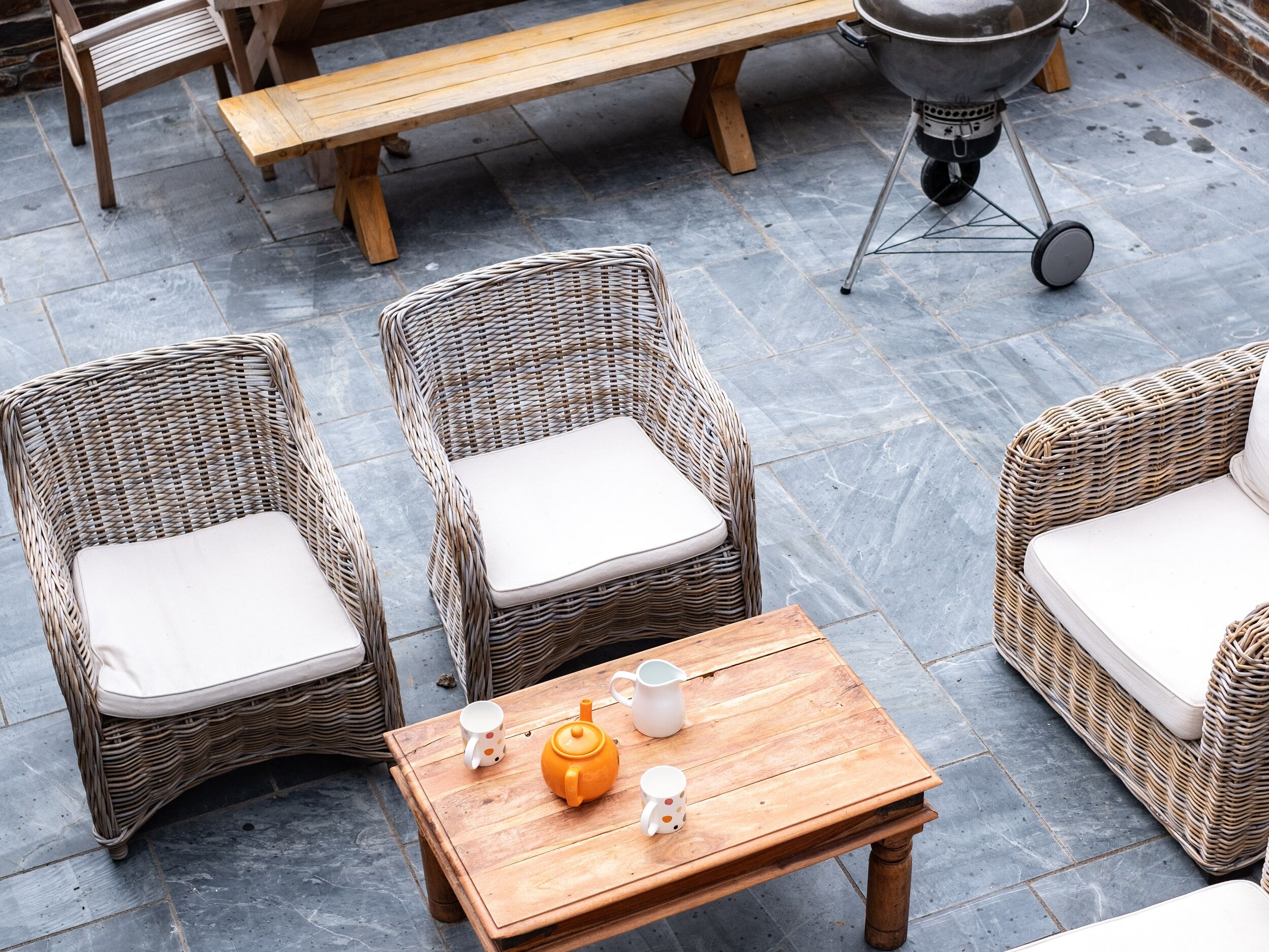 A patio area with wicker furniture, a wooden table, and a barbecue grill.