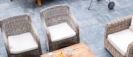 A patio area with wicker furniture, a wooden table, and a barbecue grill.