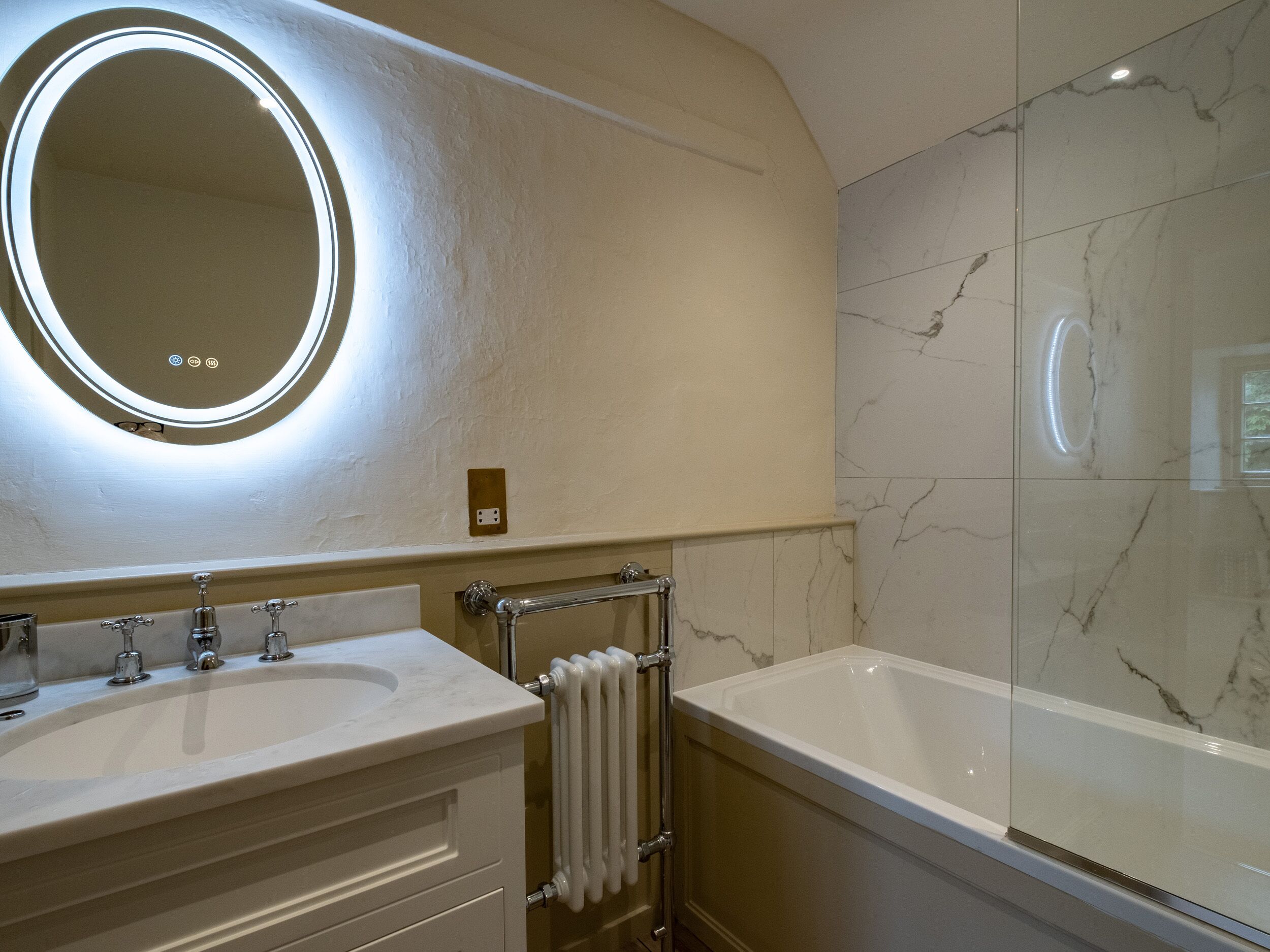 A bathroom with a double sink, a large mirror with a light, and a bathtub.