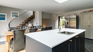 A modern kitchen with a central island, black cabinets, and a stainless steel sink. - Porthilly Greys (Wadebridge)