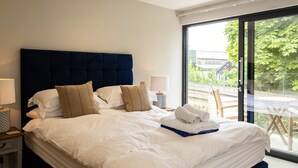 A modern hotel room with a large bed, white linens, a dark headboard, and a view of greenery outside. - Porthilly Greys (Wadebridge)