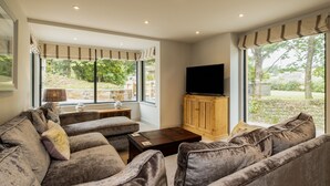 A living room with a sofa set, a wooden cabinet, and a flat-screen TV. - Porthilly Greys (Wadebridge)