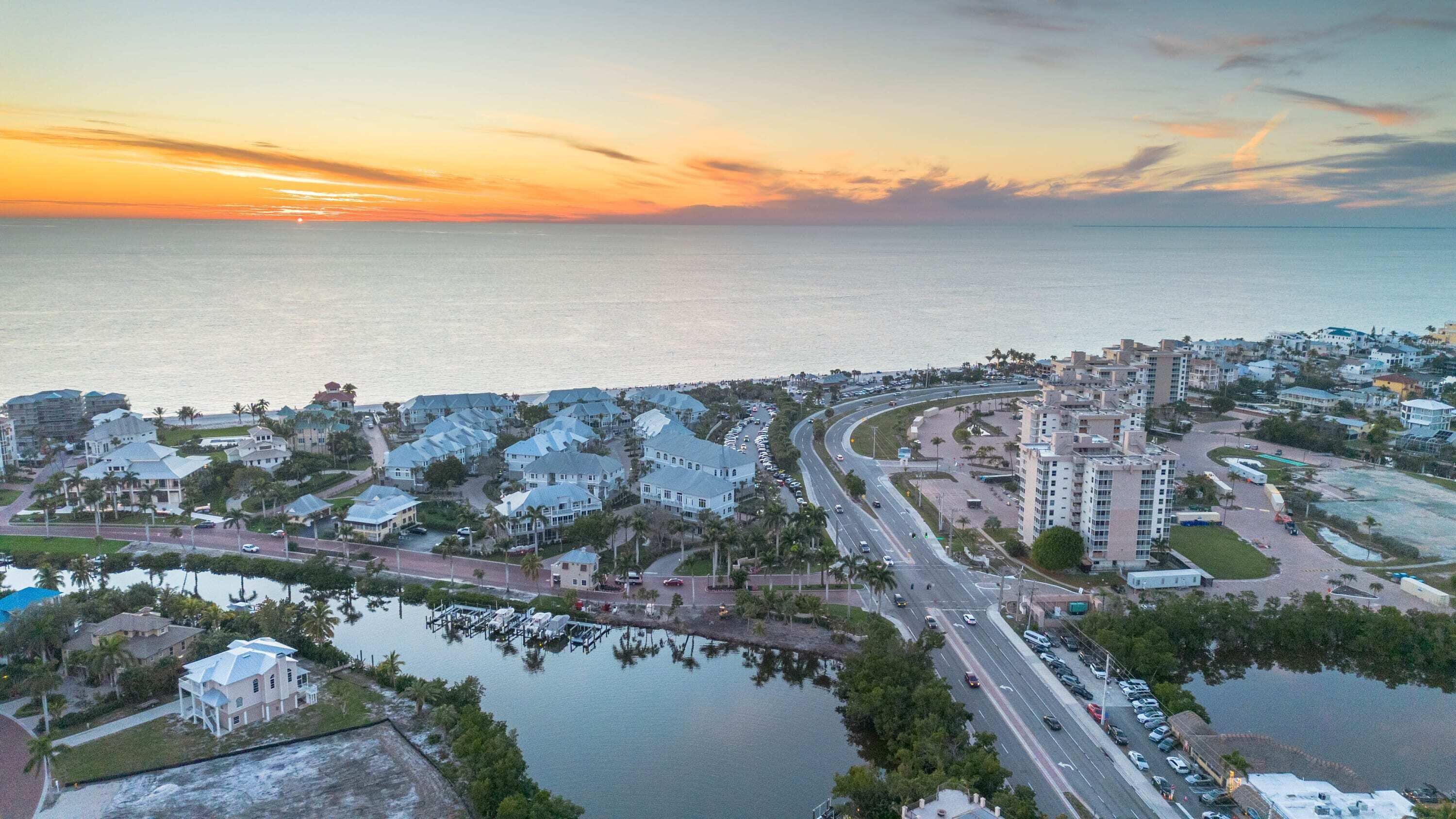 An aerial view of a coastal residential area with a marina, roads, and buildings.