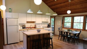 Une cuisine moderne avec des meubles en bois, un îlot central, des tabourets de bar et un coin repas comprenant une table et des chaises.