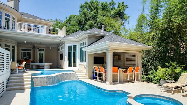 Ein Pool mit einer Senkzone, umgeben von Liegestühlen und einer überdachten Grillgegend.