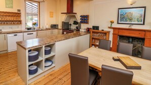 A modern kitchen with a central island, built-in shelves, a dining area with chairs, and a fireplace. - Tayview (Killin)