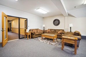 A spacious living room with a brown leather sofa set, two wooden side tables, a patterned rug, and a wall-mounted decorative plate.