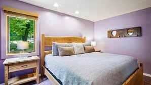 A bedroom with a wooden bed, a nightstand, a lamp, and a view of greenery through a window. - Beautiful decorated Condo, pool, hot tub, great Killington Views - Highridge B6 (Killington)