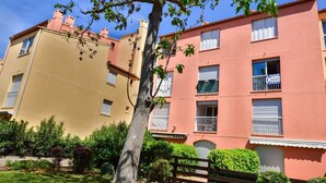 Un edificio de varios pisos con balcones, un jardín y un cartel que indica que la propiedad está en venta.